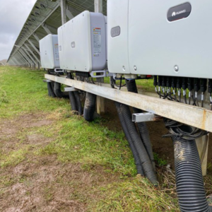 Array of sophisticated solar inverters mounted alongside a large solar farm, showcasing the modern technology used to manage and convert solar energy. The installation features robust cabling and is designed for optimal performance and durability in outdoor environments."